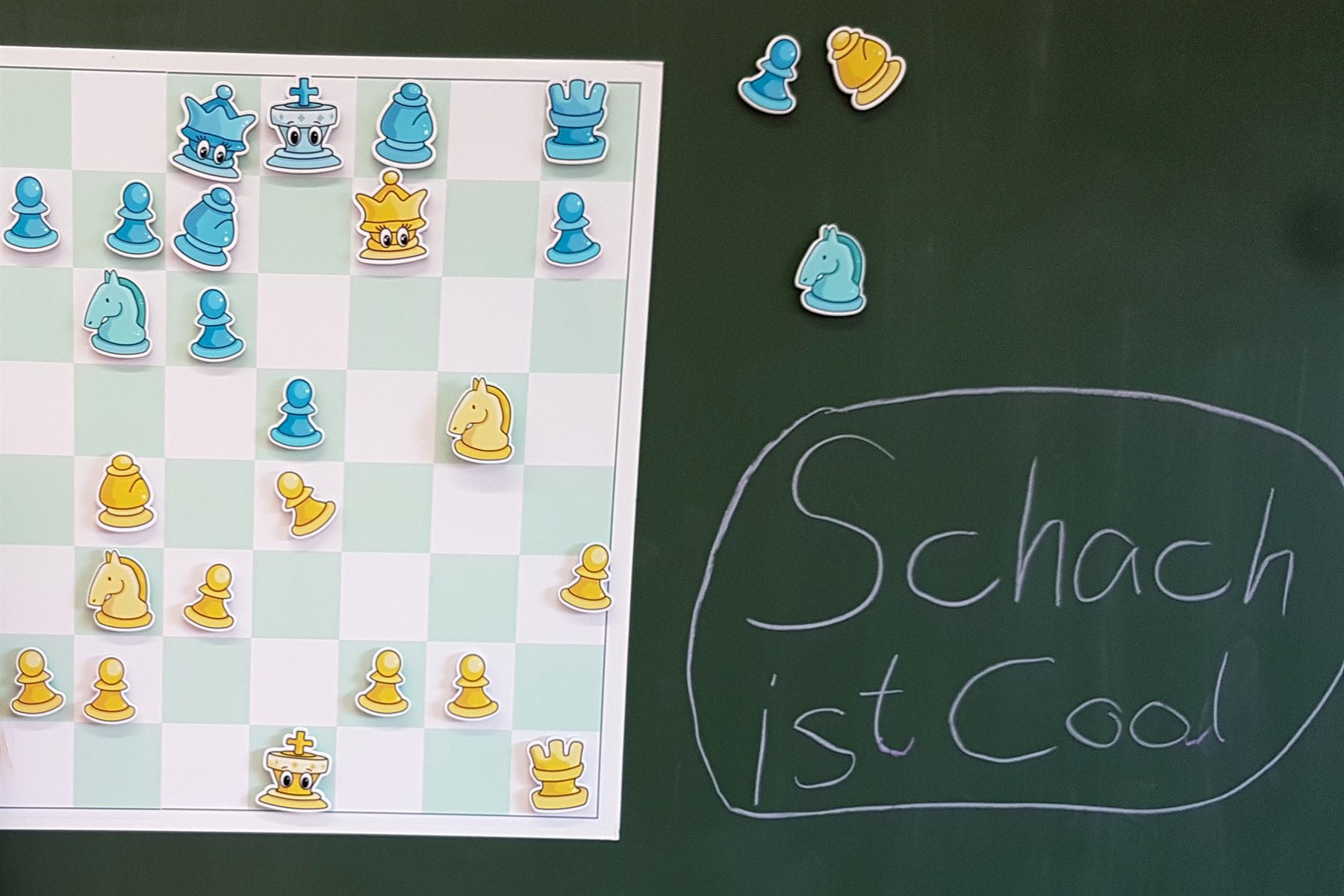 Demobrett mit kindgerechten Magnet-Schachfiguren an einer Schultafel;
                  daneben steht in Kreide „Schach ist Cool“